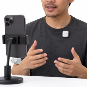 Man wearing a silver-white clip-on microphone while speaking toward a smartphone with a receiver attached against a white background